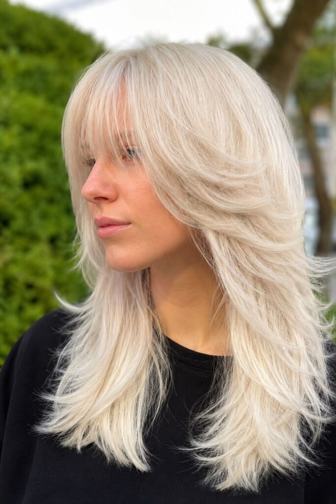 Woman with a platinum shag haircut featuring feathered layers, soft curtain bangs, and textured ends.