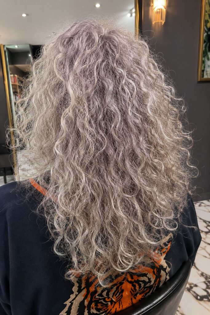 Woman with a salt and pepper shag haircut featuring natural gray curls, layered texture, and soft volume.