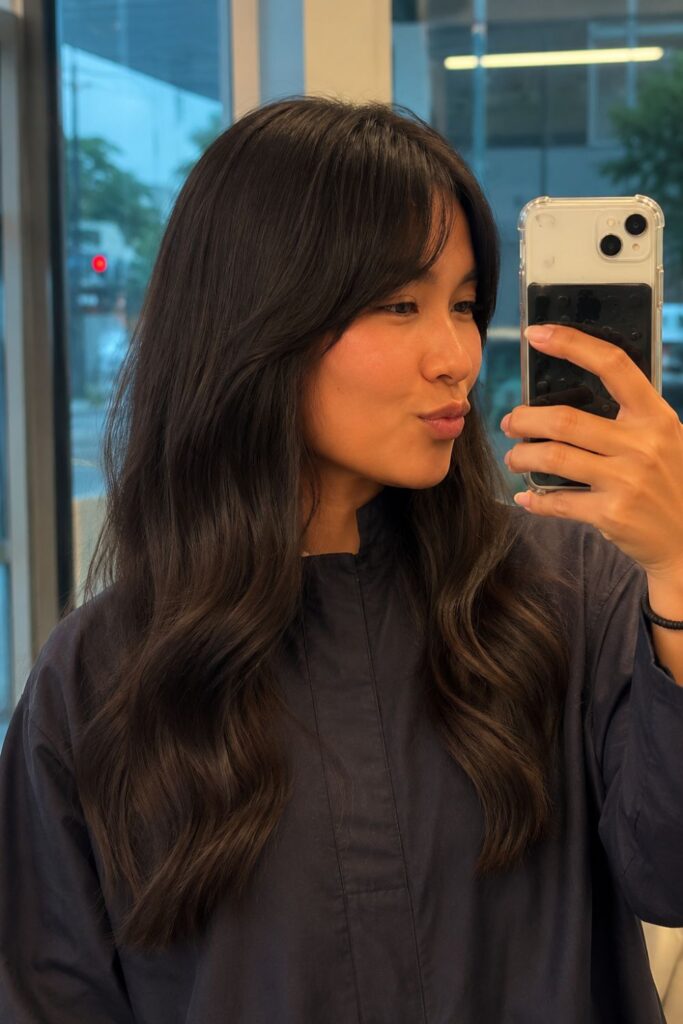 Woman with a soft brunette shag haircut featuring long textured layers, curtain bangs, and loose waves.