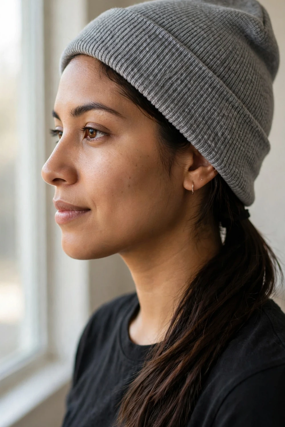 Woman with dark brown hair in a sleek low ponytail wearing a gray knit beanie