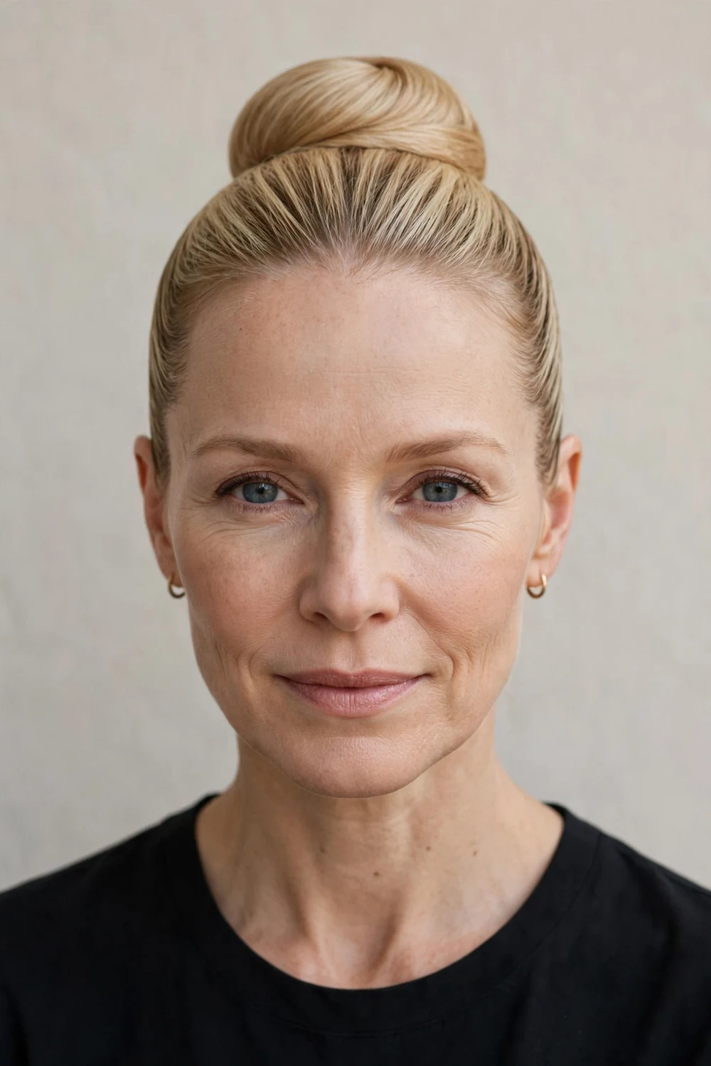 Blonde woman in her 40s with a neat elegant ballet bun at the crown, sleek pulled-back sides and refined dancer-like look