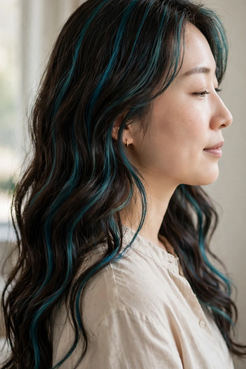 Woman with dark brunette hair featuring teal blue streaks in long waves