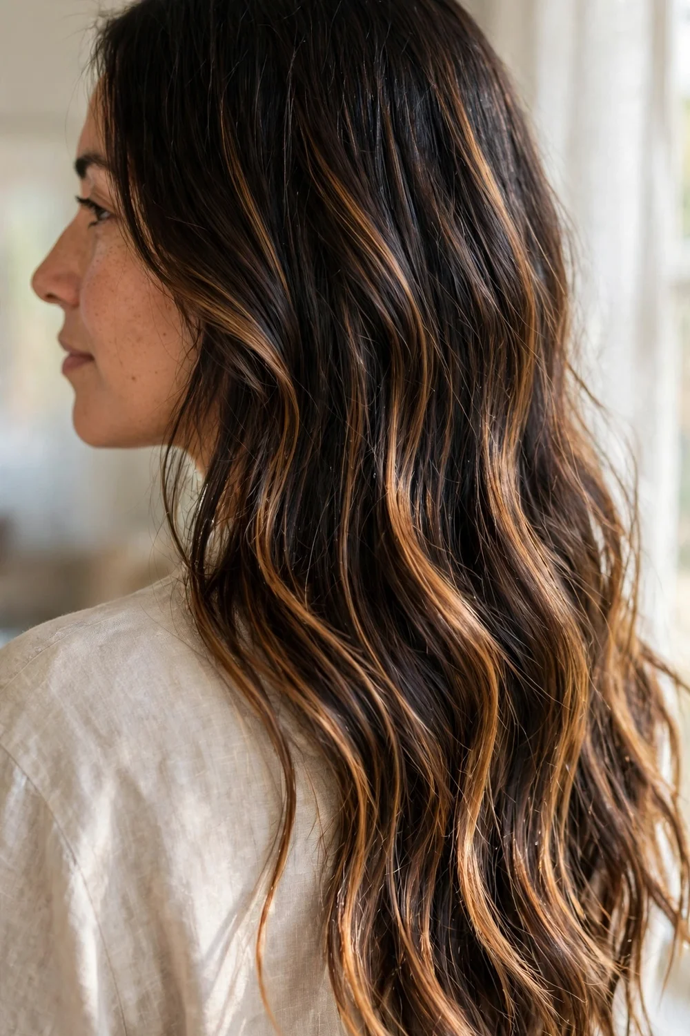 Woman with dark brown long hair and caramel balayage ribbons, back three-quarter view