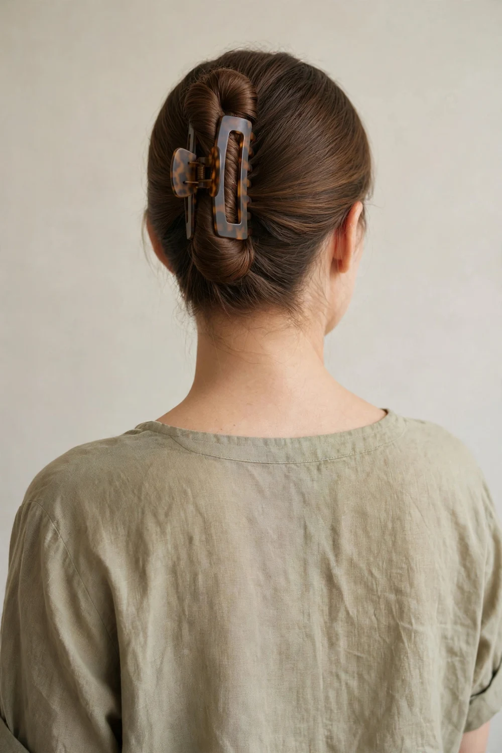 Back view of a woman with chestnut straight long hair in a French twist held by a large claw clip
