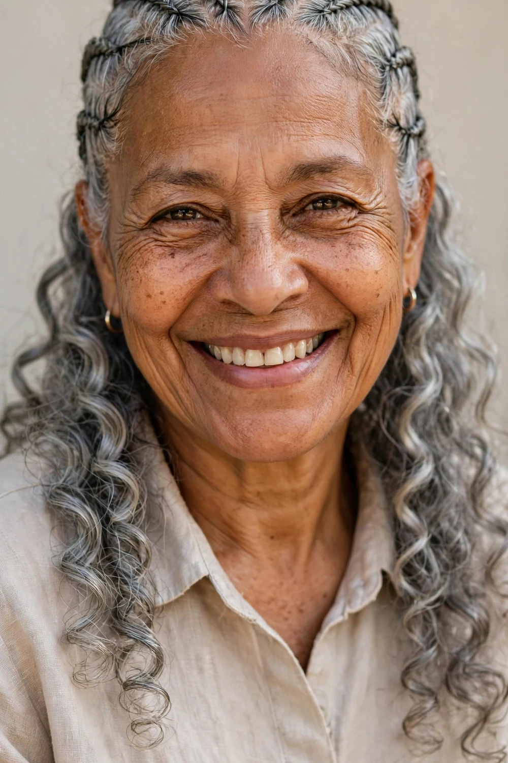 Older woman in her 60s with front gray cornrows and loose silver spiral curls at the back