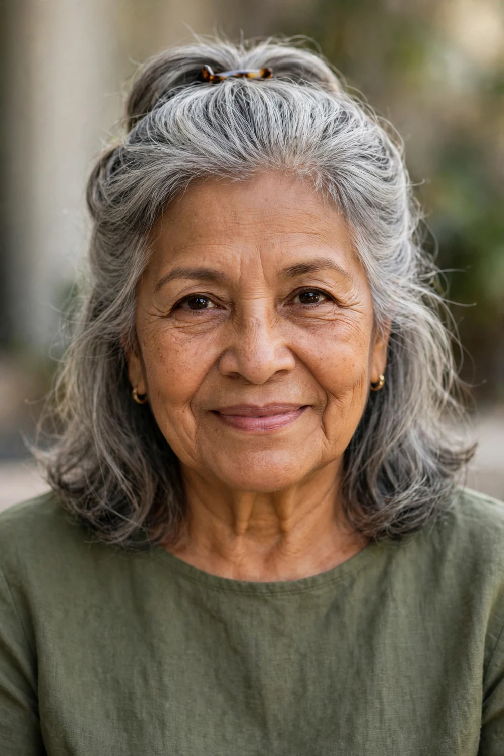 Latina woman in her mid 70s with shoulder-length gray hair half-up and pinned back