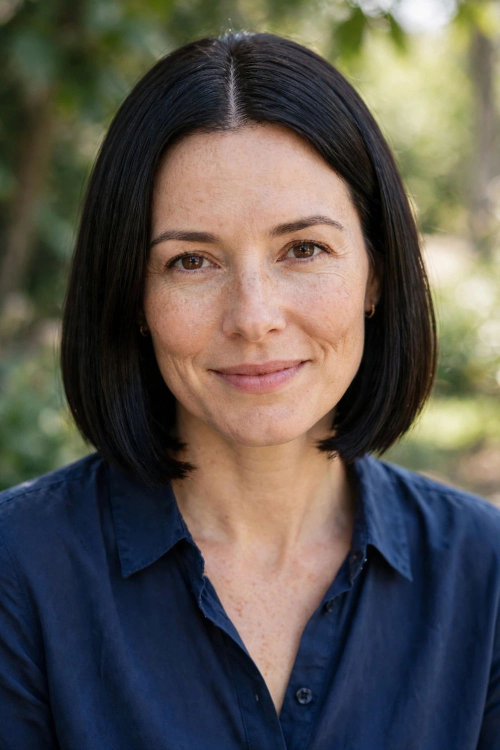 Woman in her late 30s with fair skin wearing a straight black blunt bob with a center part ending at the jawline