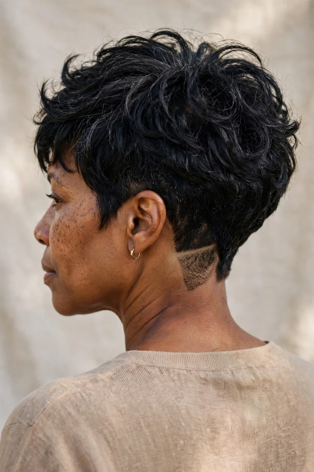 Woman with thick black hair wearing a layered pixie with a shaved nape undercut